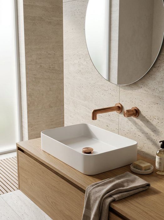 Grifo de baño de pared oro rosa en un baño de travertino: Idun sobre un lavabo blanco en un mueble de roble