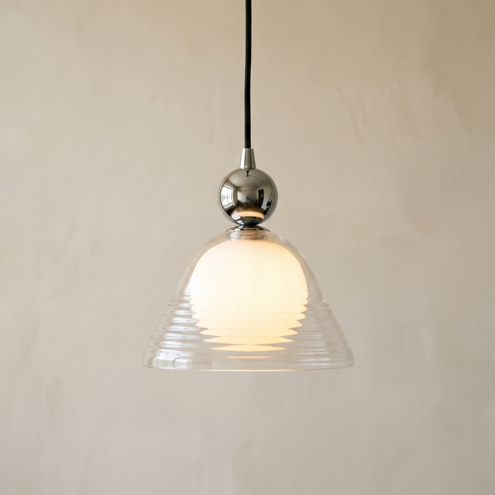 Hedda dimmable pendant light lit against a warm plaster wall, showing the clear ribbed bell over the opal inner globe